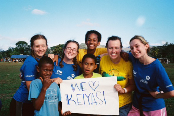 A group of people in a park, smiling and holding a white sign that says ‘We love Keiyasi’